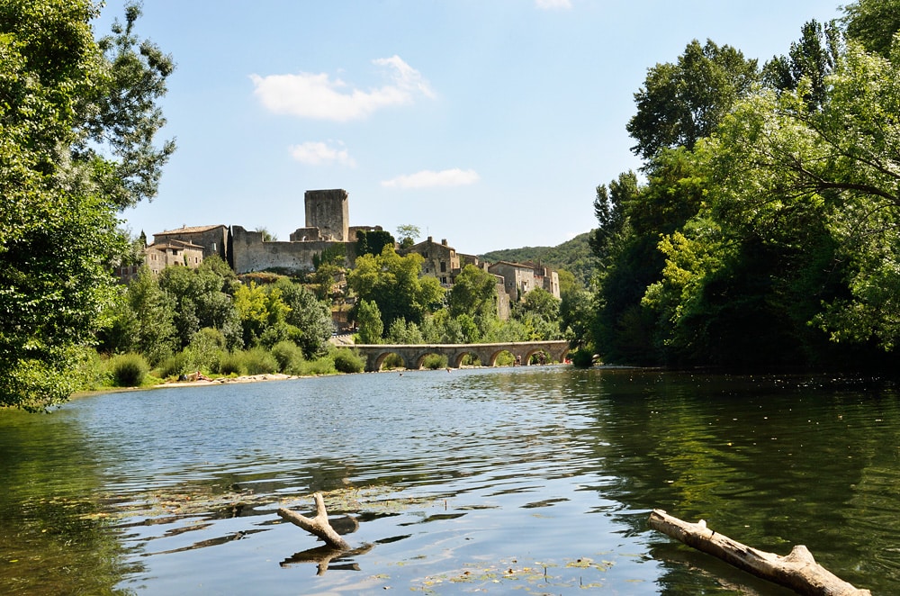 Vue sur le village médiéval fortifié de Castelfranc perché au-dessus d'une rivière calme avec un pont en arc en pierre.
