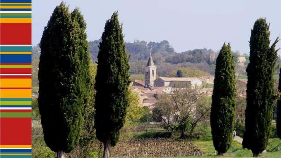 Quatre cyprès sombres bordent un paysage provençal avec un village, son clocher, et des vignes au printemps. Bandeau aux couleurs de la Provence à gauche.