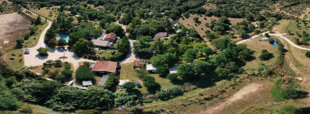Domaine boisé : vue aérienne de gîtes ruraux et d'un camping avec piscine bleue, parking et emplacements pour caravanes.
