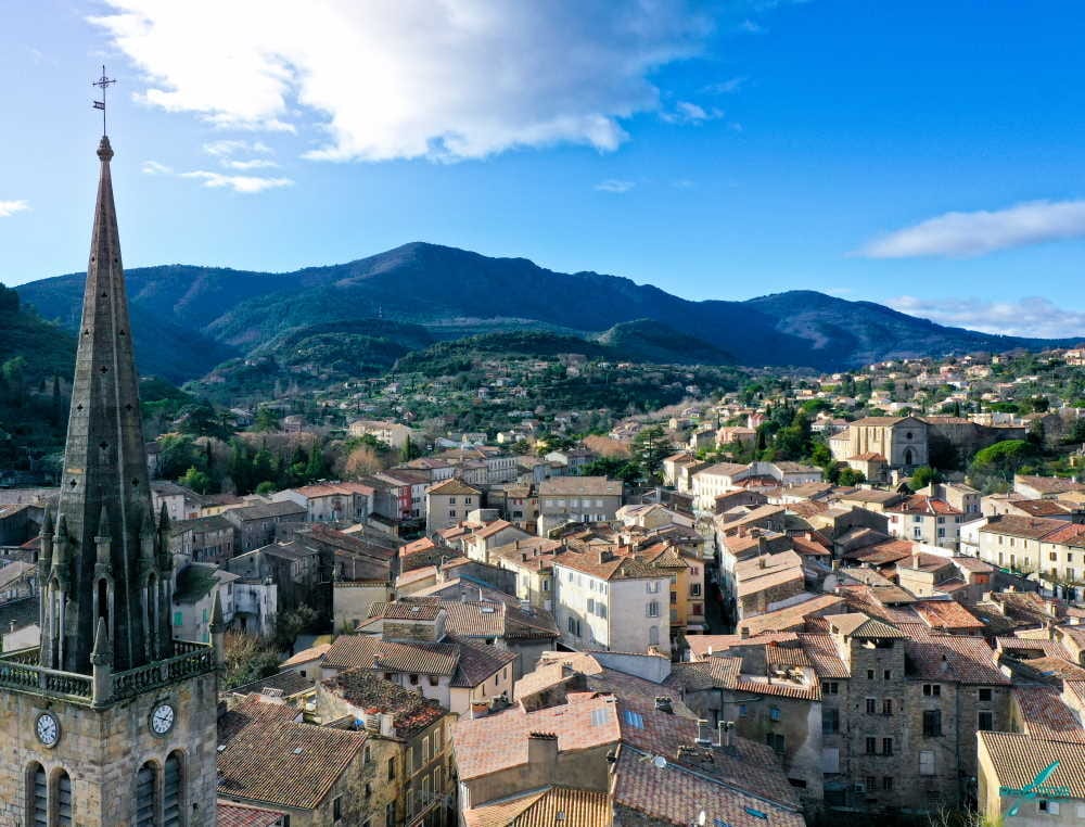 Vue plongeante d'un village historique aux toits ocre. Le clocher principal et les montagnes bleues du sud-est dominent le paysage.