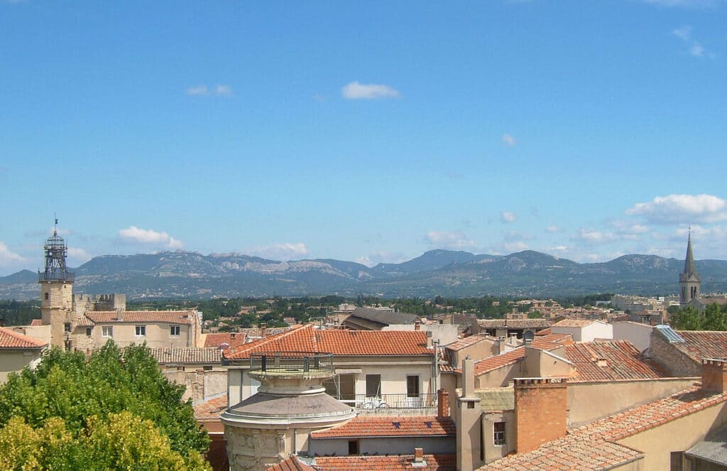Vue panoramique de Provence: toits rouges, clocher médiéval et rotunda moderne. Montagnes calcaires sous un ciel bleu d'été.
