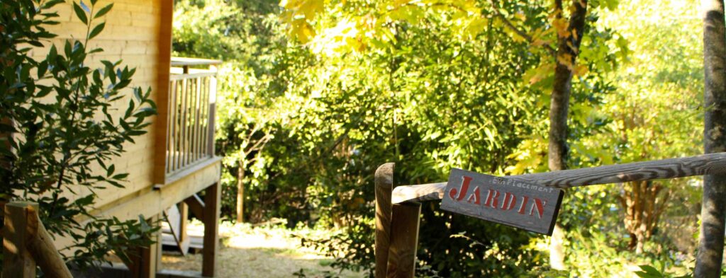 Cabane en bois et sa terrasse surplombant un jardin luxuriant, avec un panneau en bois marqué Jardin.