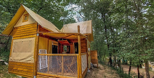 Lodge de glamping en bois avec toit en toile et terrasse sécurisée dans une forêt luxuriante.