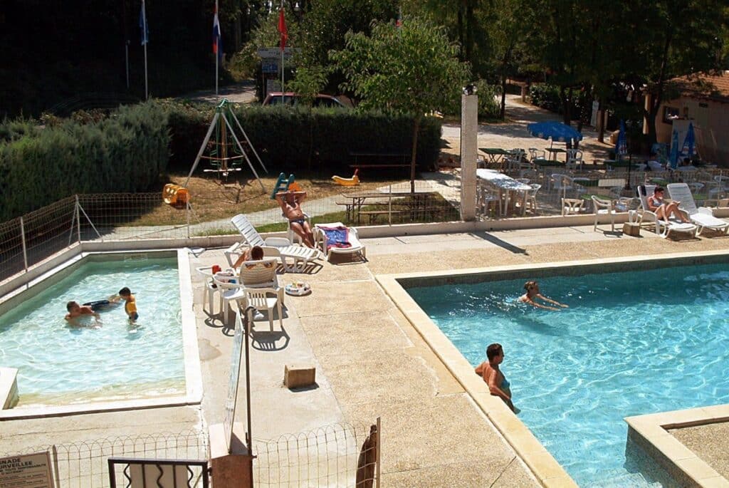 Familles profitant de la piscine et de l'aire de jeux d'un camping ensoleillé pendant les vacances d'été.