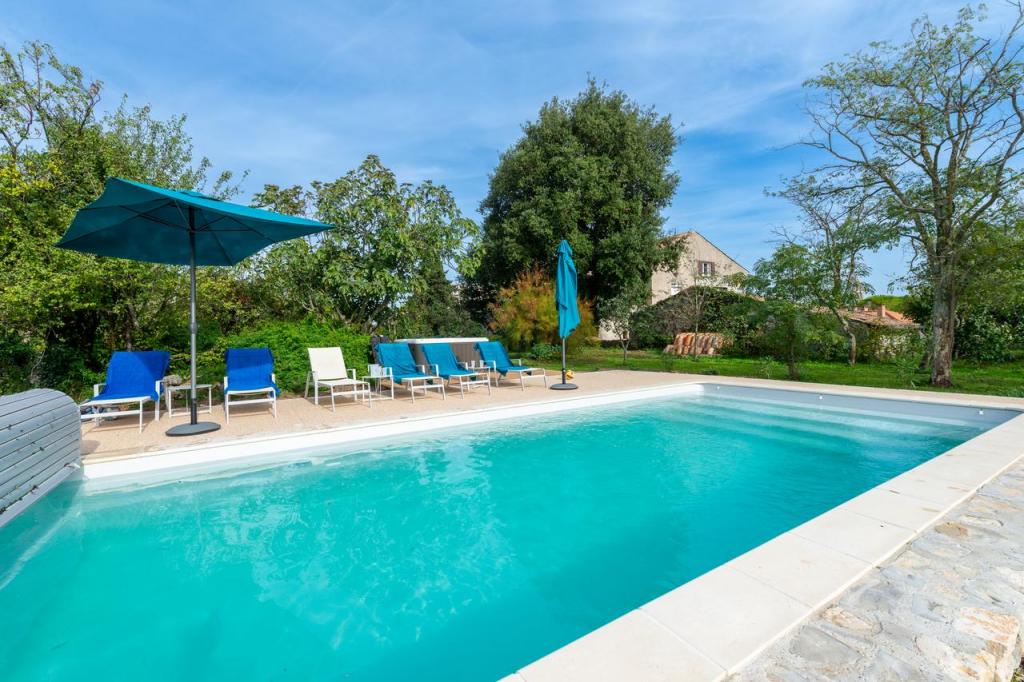 Piscine turquoise, transats et parasols sur une terrasse ensoleillée entourée d'un jardin verdoyant.