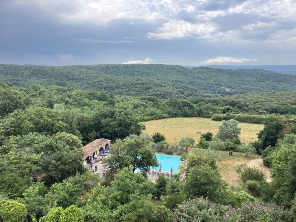 Piscine avec pool house au cœur d'une forêt dense et de collines verdoyantes sous un ciel orageux.