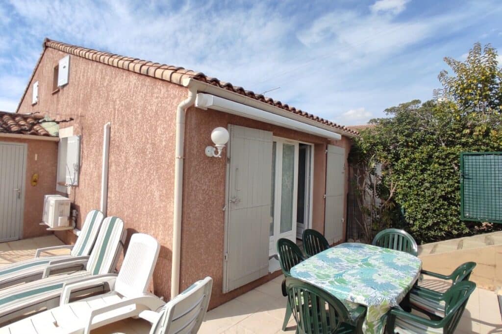 Terrasse avec mobilier de jardin, store banne et transats devant une maison provençale au crépi rose.
