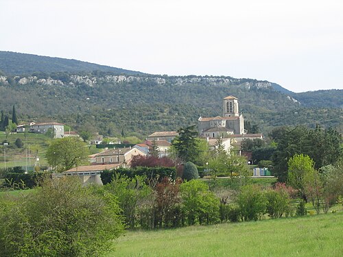 Village pittoresque avec église en pierre au pied d'une colline rocheuse et paysages verdoyants.