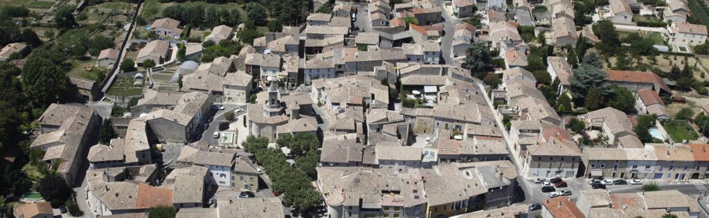 Vue aérienne d'un village pittoresque aux toits de tuiles orangées entouré de verdure avec son église centrale.